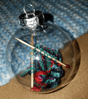 miniature knitting project on toothpick needles inside a clear glass ball ornament