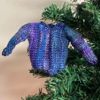 closeup of tiny Iced Sweater in blue and purple yarn fastened with wire as an ornament on a Christmas tree