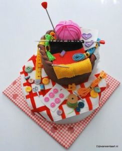 knitted chocolate cake with partially knitted scarf and ball of yarn on top any buttons, thread, and other stitching notions scattered around